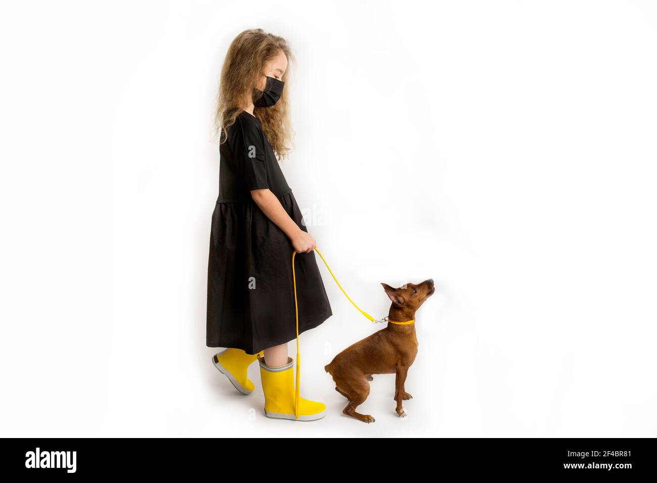 Une fille dans un masque antiviral protecteur noir marche le chien. Nouvelle réalité de la vie durant la pandémie COVID-19. Banque D'Images