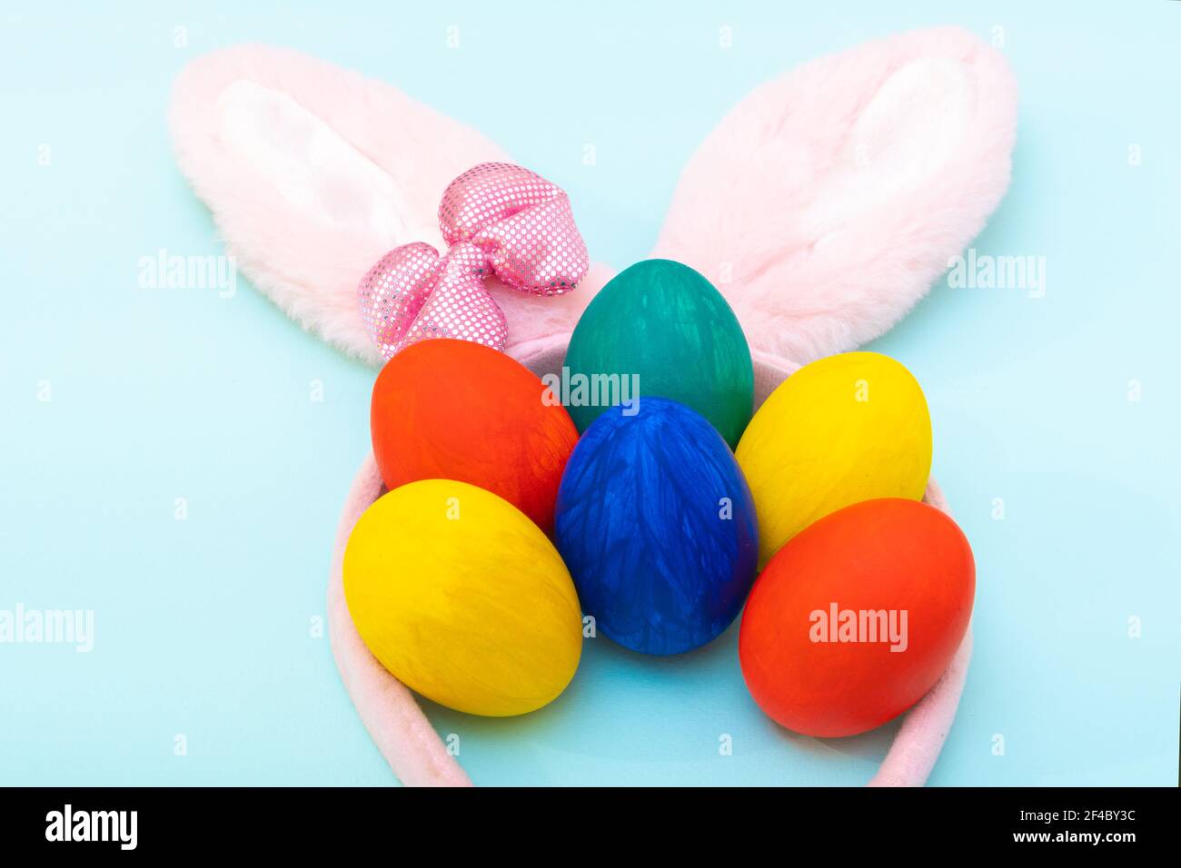 Concept joyeuses Pâques. Œufs de Pâques peints à la main et oreilles de lapin roses sur fond bleu, gros plan. Carte de Pâques minimaliste Banque D'Images