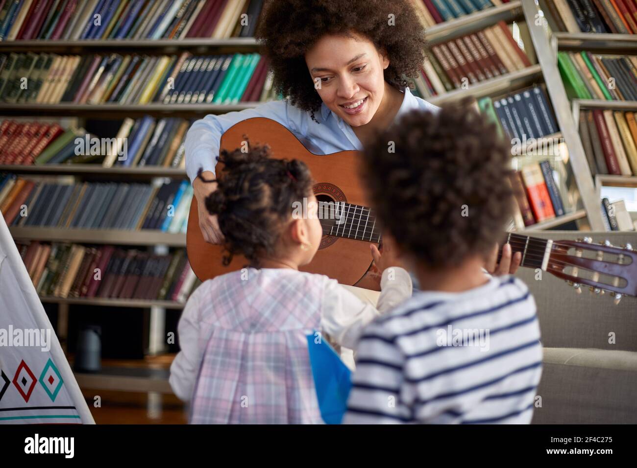 Les petits enfants sont curieux de la guitare que leur mère joue pour eux dans une atmosphère détendue à la maison. Famille, maison, temps de jeu Banque D'Images