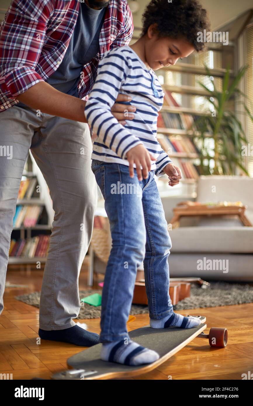Un père dans une atmosphère ludique à la maison enseigne à son fils comment monter à bord d'un skateboard. Famille, maison, temps de jeu Banque D'Images