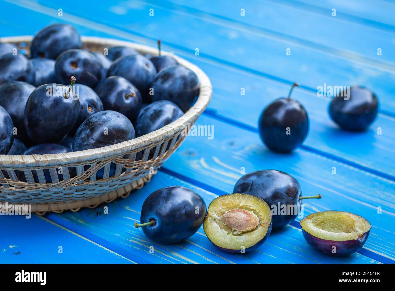 Prunes organiques dans le panier sur la table. Fruits frais récoltés. Gros plan sur les prunes mûres coupées en deux Banque D'Images