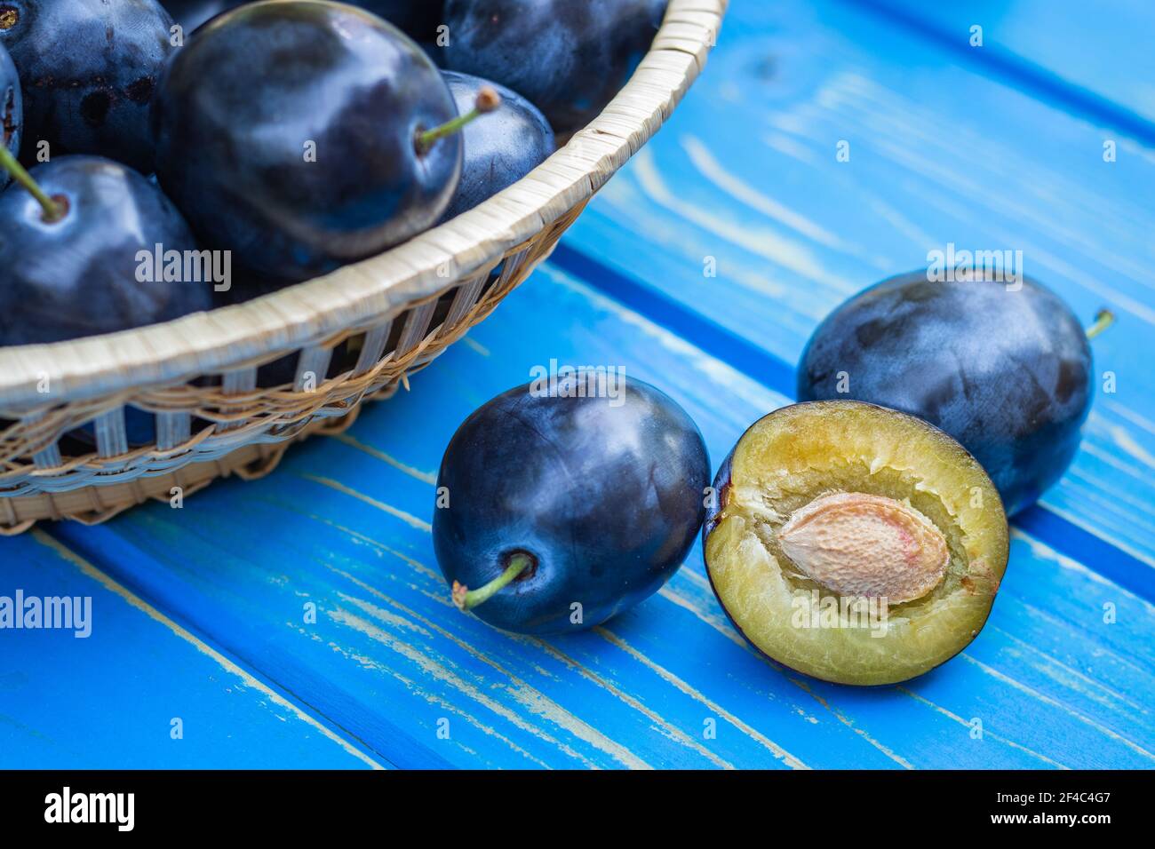 Prunes sur table en bois bleu. Fruits mûrs frais récoltés. Vue rapprochée des prunes coupées en deux Banque D'Images