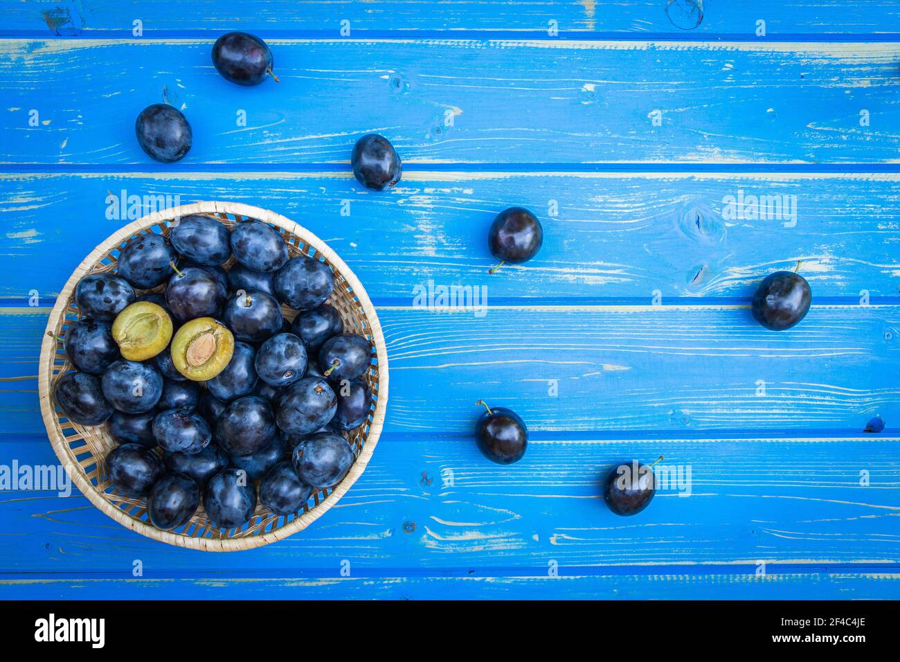 Prunes en panier sur table en bois bleu, directement au-dessus, à plat. Fruits frais récoltés. Banque D'Images