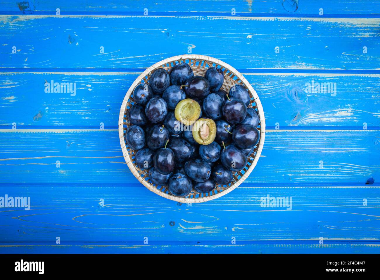 Prunes mûres dans un bol sur une table en bois bleu, à plat. Fruits prune fraîchement récoltés Banque D'Images