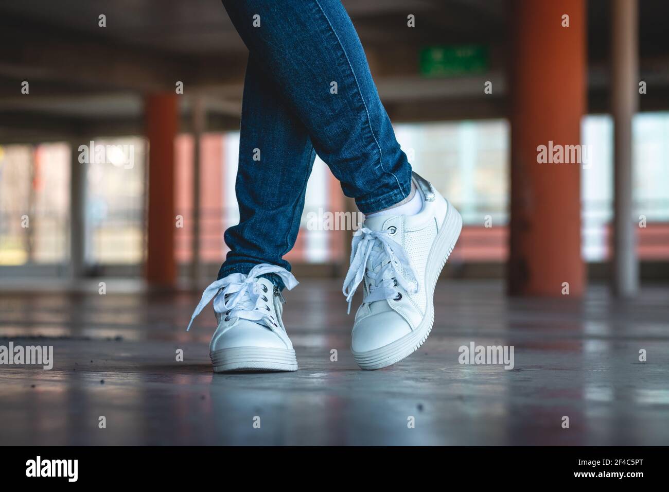 Femme avec des baskets blanches dans un parking public. Mode concept. Les  jambes fines des femmes portent un Jean et des chaussures de sport dans le  parking Photo Stock - Alamy