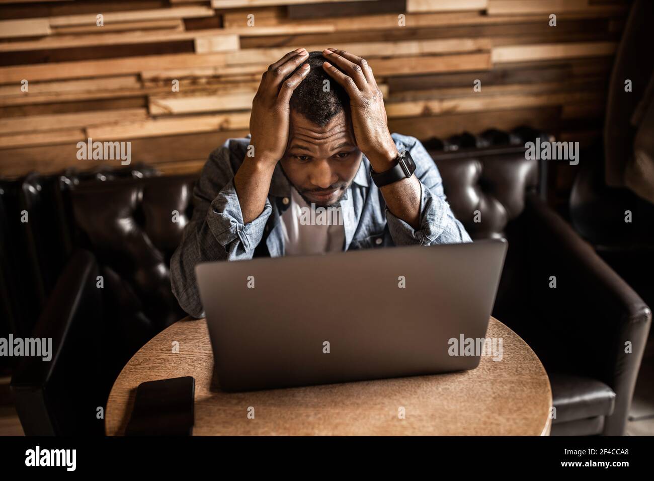 Un jeune Afro-américain malheureux tenant la tête entre les mains, un homme d'affaires fatigué assis au bureau avec un ordinateur portable se sentant épuisé, des problèmes financiers Banque D'Images