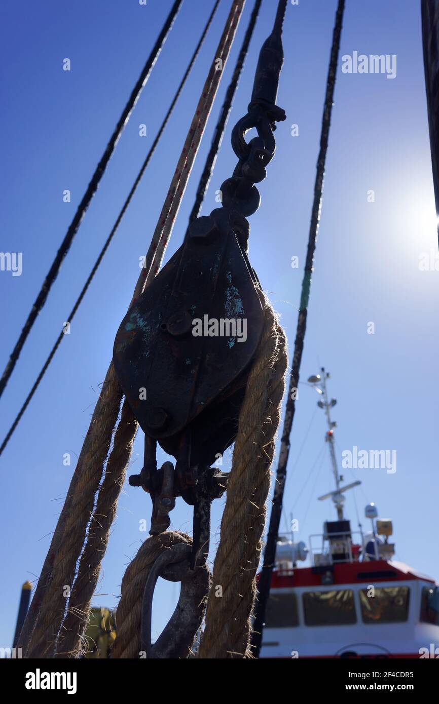 Un bloc et un matériel anciens utilisés pour transporter des voiles sur un vieux voilier en bois recréé contre un bateau à moteur moderne. Banque D'Images