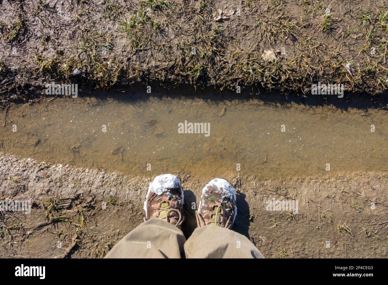 Flaque d'eau, sillon printemps, neige sur les orteils des chaussures, vue d'en haut chaussures de marche Banque D'Images