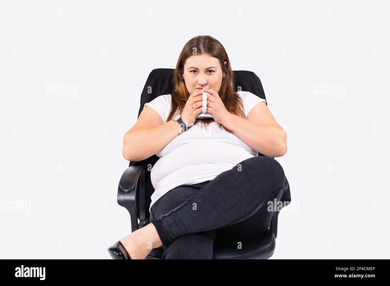Photo d'incroyable belle grande femme, femme d'affaires tient les bras mains verre blanc café chaud ou thé regardant l'appareil photo, s'asseoir grand bureau chaise confortable Banque D'Images