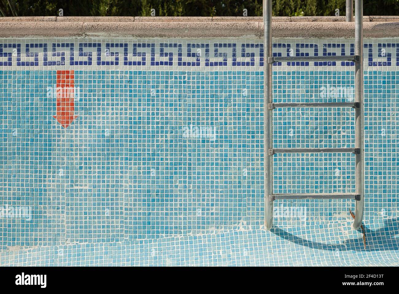 Piscine carrelée sans eau avec une échelle et une flèche rouge vers le bas. Arrière-plan texturé. Banque D'Images