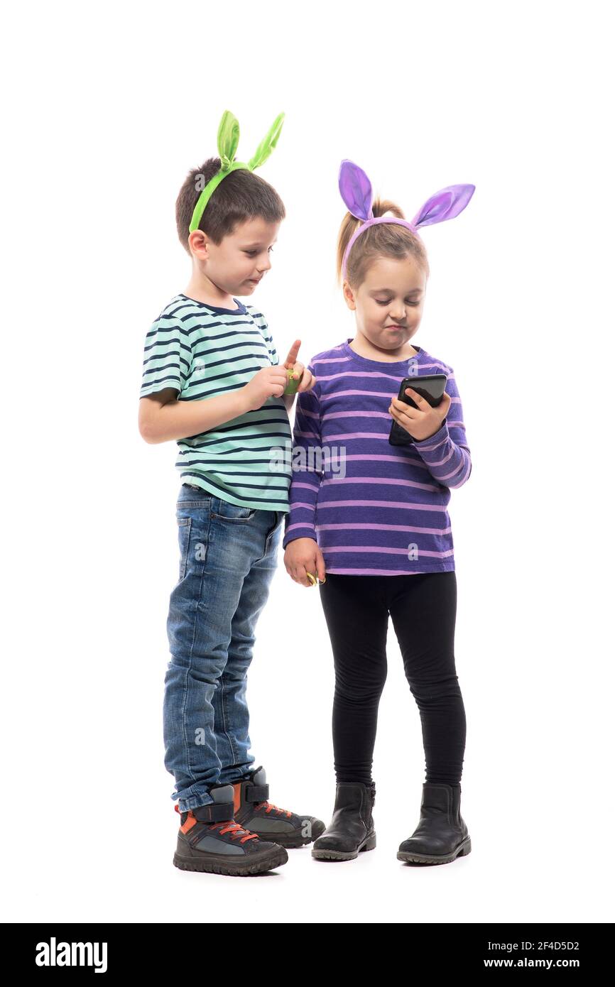 Les enfants de Pâques avec chapeau de lapin regardent et tiennent le smartphone à l'attention. Corps entier isolé sur fond blanc Banque D'Images