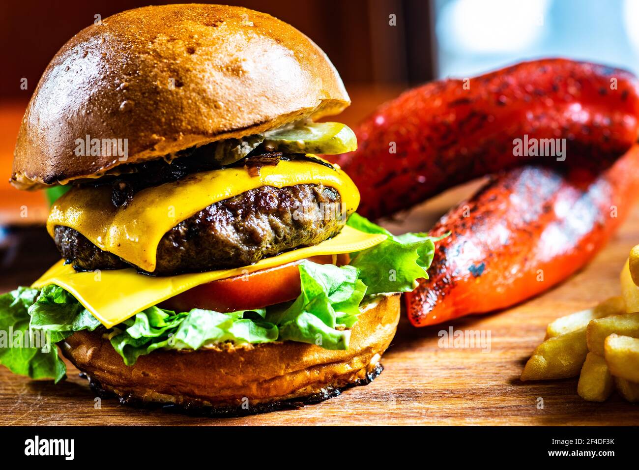 Gros plan d'un cheeseburger à la tomate, au cornichon et à la laitue, servi avec des frites et des poivrons rouges rôtis Banque D'Images