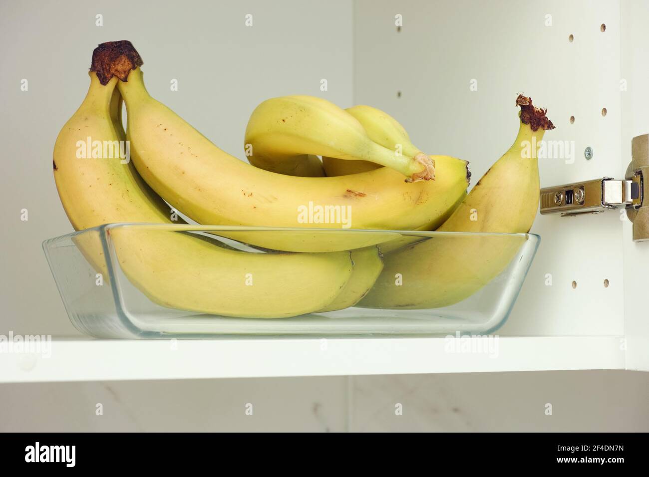 Bouquet de bananes dans un récipient en verre qui est dans un placard de cuisine. Gros plan. Banque D'Images