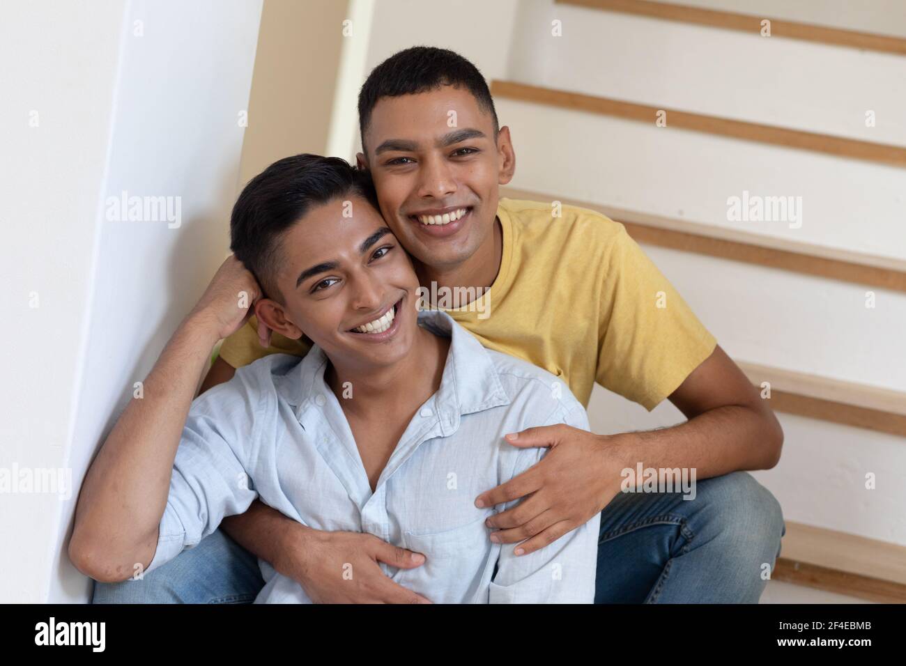 Portrait d'un couple gay masculin varié assis dans un escalier à l'appareil photo et souriant Banque D'Images