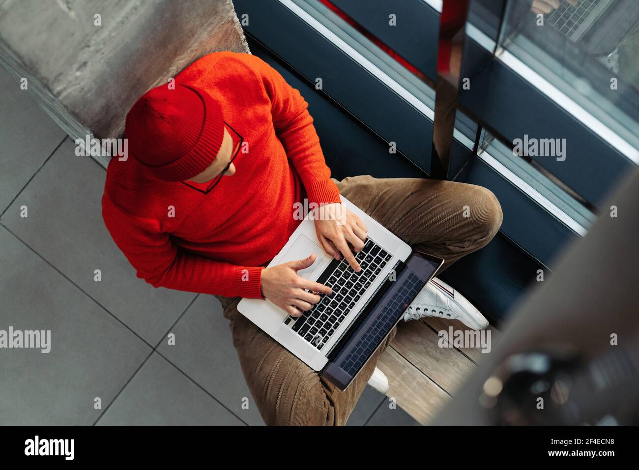 Indépendant homme assis sur le banc à côté de jambes de fenêtre croisées, travail en ligne sur ordinateur portable. Travail à distance Banque D'Images