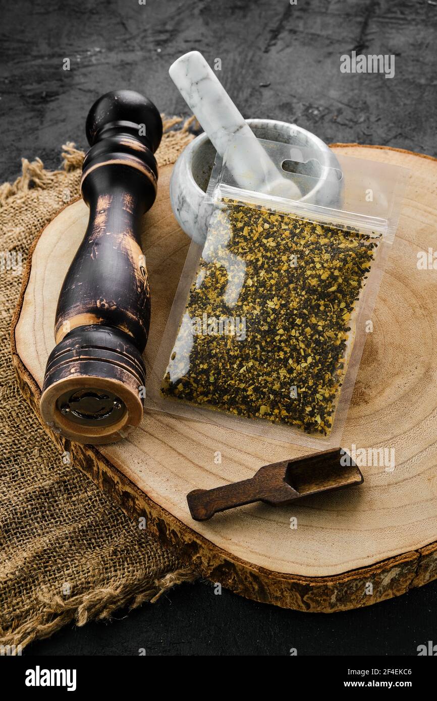 Section en bois avec poivre de citron dans un emballage en plastique et mortier et moulin à pierre Banque D'Images