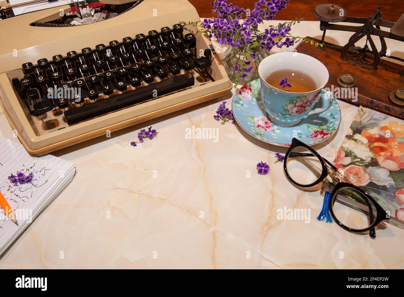 Machine à écrire manuelle rétro à l'ancienne sur un bureau avec tasse, bloc-notes, lunettes, pèse-lettres et fleurs avec espace de copie. Banque D'Images