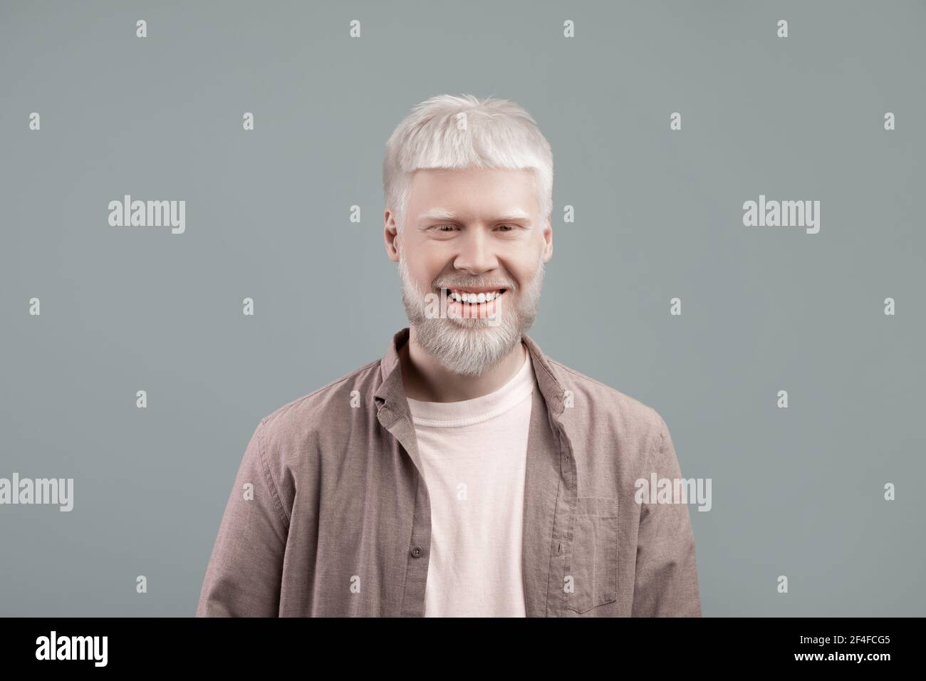Homme d'albino heureux avec la peau blanche et les cheveux posant avec sourire assuré sur fond gris studio Banque D'Images