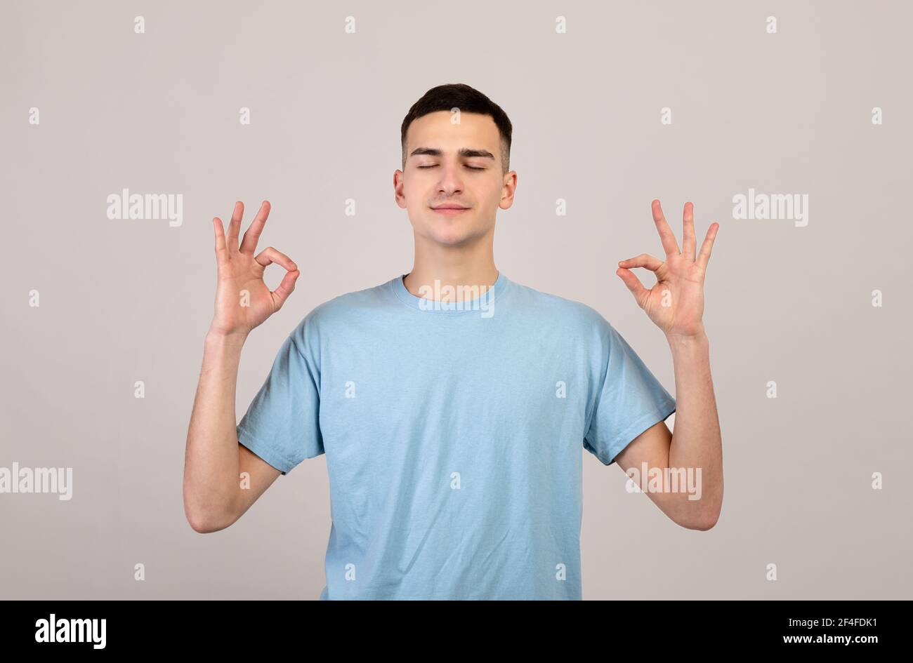 Concept de gestion du stress. Paisible jeune homme méditant, trouvant l'équilibre intérieur et l'harmonie sur fond gris studio Banque D'Images