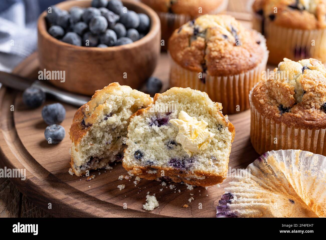 Muffin aux myrtilles coupé en deux avec beurre et baies et muffins en arrière-plan sur un plateau en bois Banque D'Images