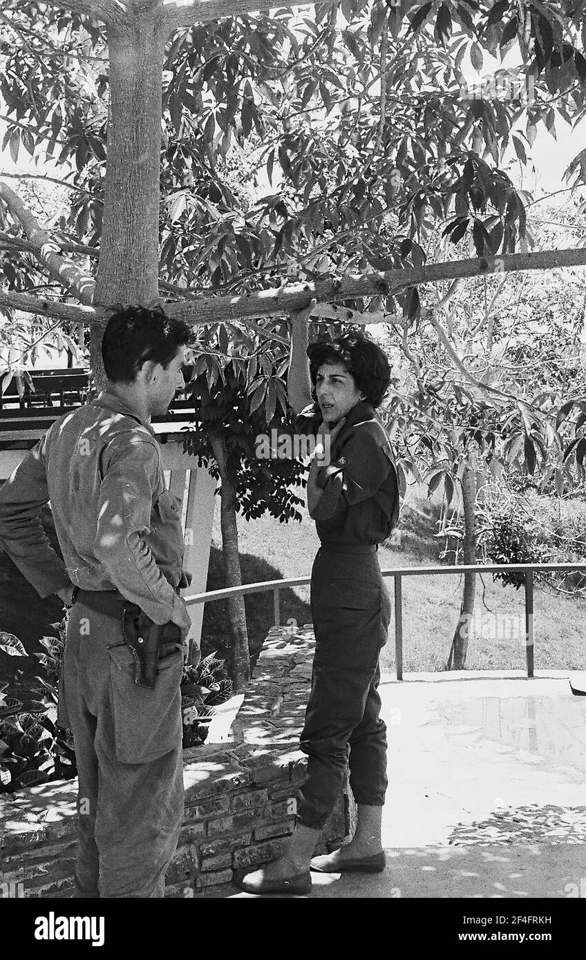 Photo de profil pleine longueur de Celia Sanchez Manduley, debout sous un arbre avec sa main accrochée autour d'une branche basse, parlant avec un administrateur armé et en uniforme au parc national de la Guira, Pinar del Rio, Cuba, 1964. De la collection de photographies Deena Stryker. () Banque D'Images