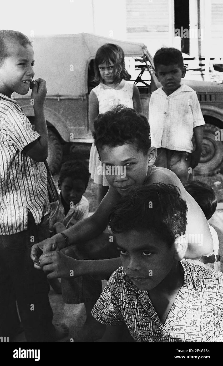Un groupe d'enfants se détendent à l'extérieur parmi les véhicules en plein soleil, Biran, Cuba, province de Holguin, 1963. De la collection de photographies Deena Stryker. () Banque D'Images