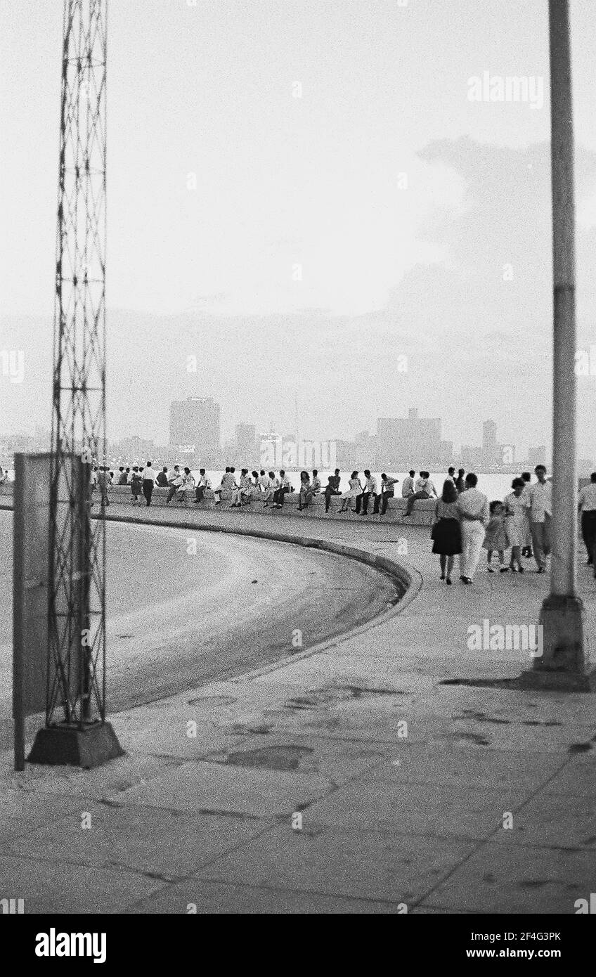 Personnes marchant sur le trottoir et assis sur un digue surplombant la ville et le port, le Malecon (Avenida de Maceo), la Havane, Cuba, 1964. De la collection de photographies Deena Stryker. () Banque D'Images