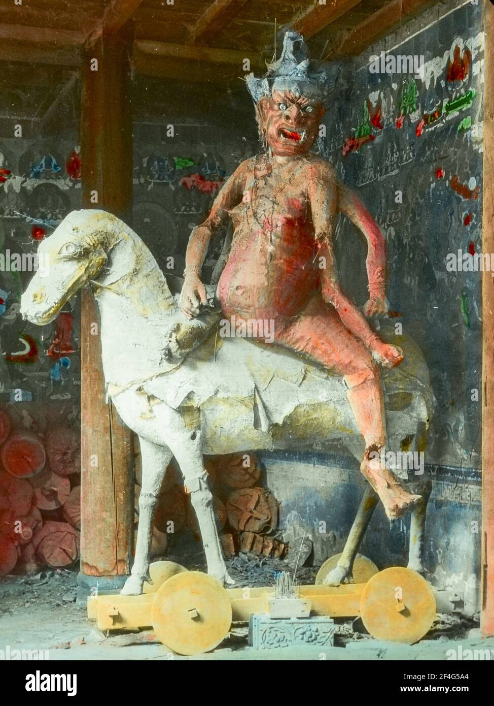 Sculpture de Yama, le roi de l'Enfer, représentée comme un démon à peau rouge, multi-armé, à cheval à roues, avec un mur peint en arrière-plan, Sichuan, Chine, 1917. De la collection de photographies Sidney D. Gamble. () Banque D'Images