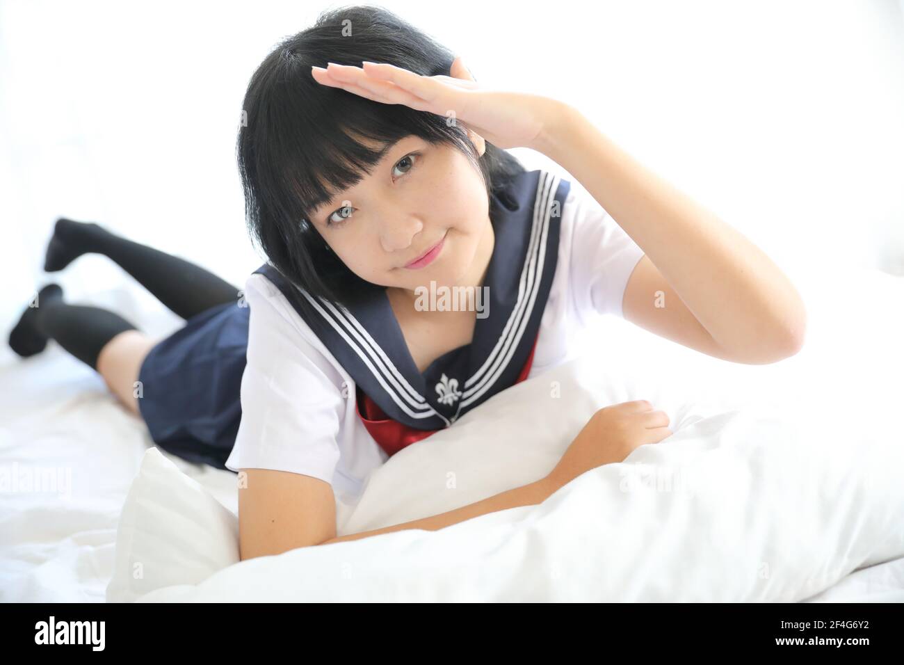 Portrait d'une fille d'école japonaise dans une chambre de lit aux tons blancs Banque D'Images