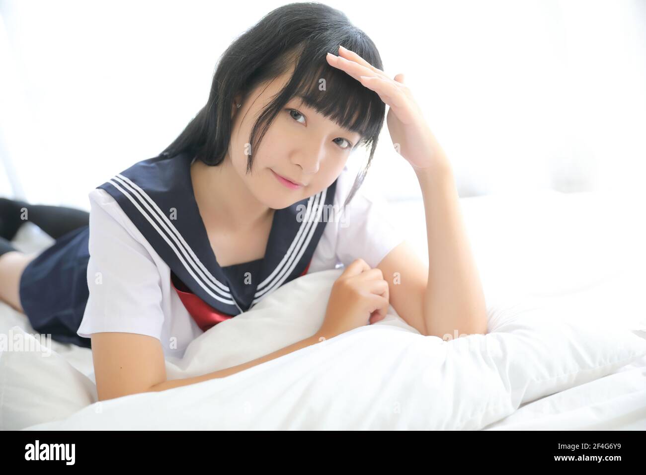 Portrait d'une fille d'école japonaise dans une chambre de lit aux tons blancs Banque D'Images