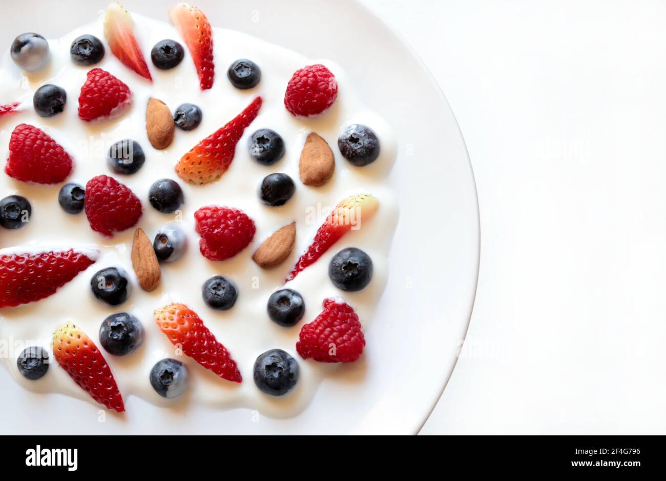 Yaourt et fruits. Yaourt aux myrtilles, fraises, framboises et amandes sur fond blanc. Directement au-dessus. Banque D'Images