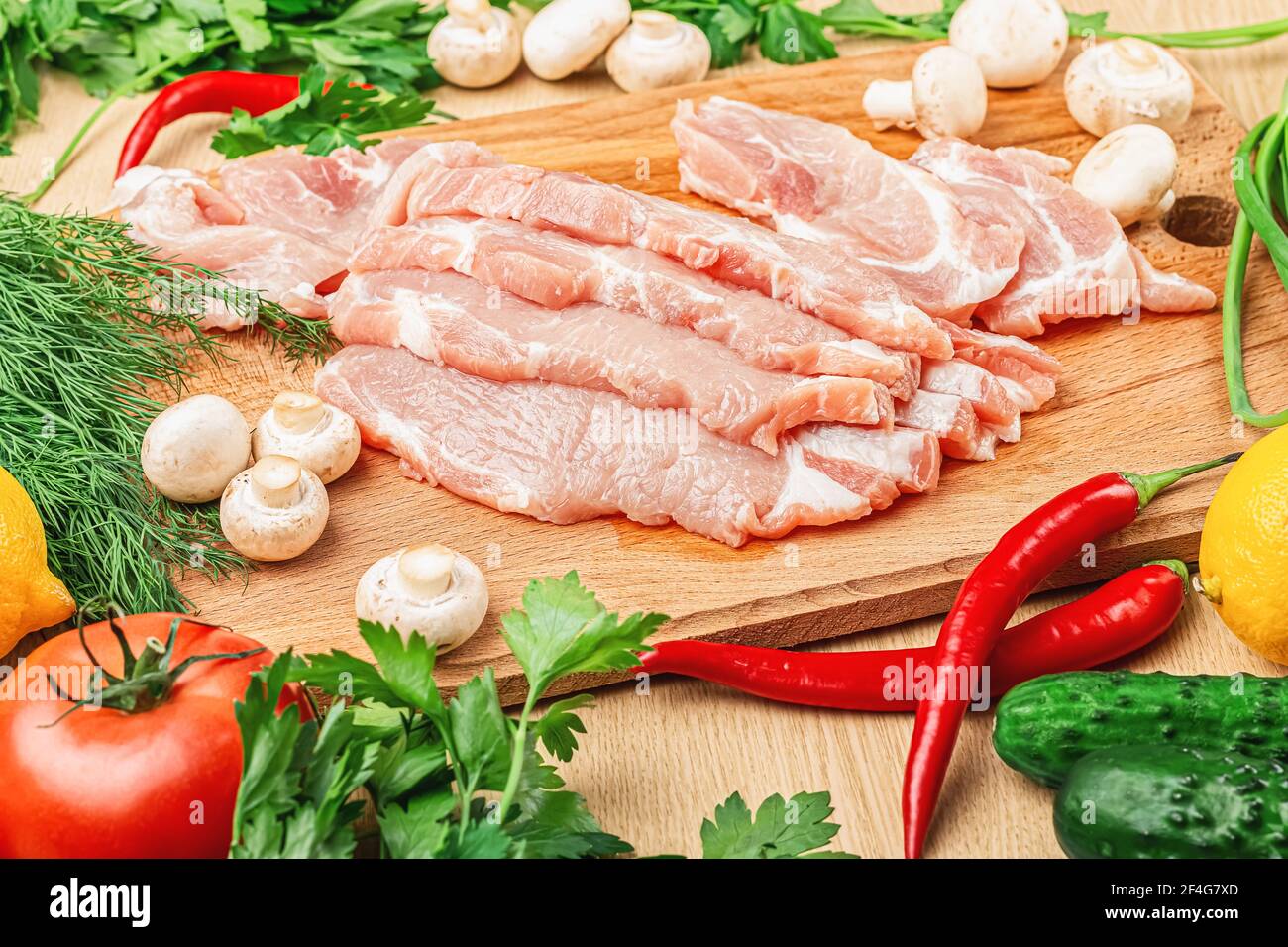 La viande de porc fraîche et crue est coupée en gros morceaux. Préparé pour la friture, la cuisson. Sur la table sont les citrons, les tomates, les poivrons chauds, les champignons, les oignons verts, pa Banque D'Images