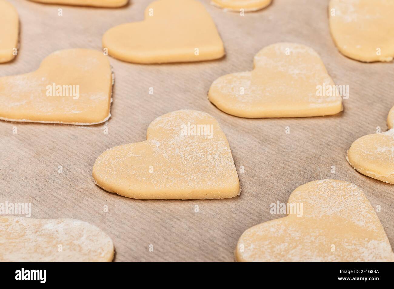 Les biscuits sablés faits maison en forme de coeur sont soigneusement disposés sur du parchemin dans la farine. Gros plan, vue de dessus et vue latérale. Banque D'Images