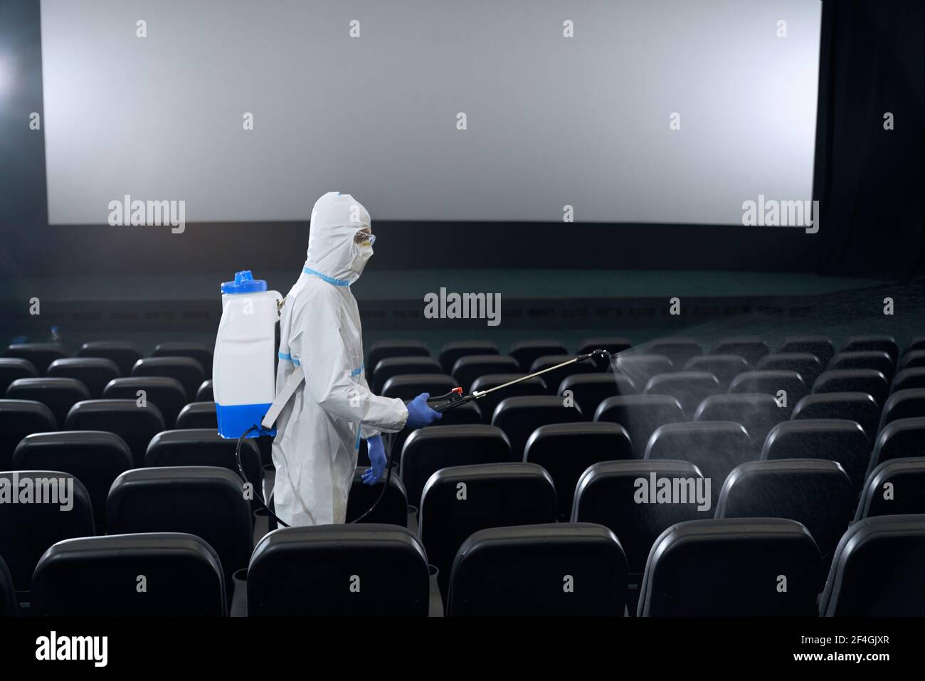 Travailleur dans les vêtements de protection blancs de fabrication désinfectez avec l'équipement spécial dans le hall de cinéma. Concept de désinfection. Banque D'Images