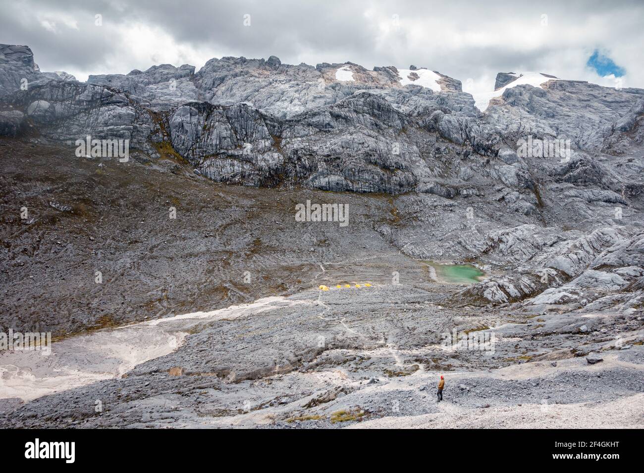 Un grimpeur mâle pendant l'expédition regardant le camp de base de haute altitude de la Pyramide Carstensz (Puncak Jaya) avec tentes de camping jaunes, lac vert et neige Banque D'Images