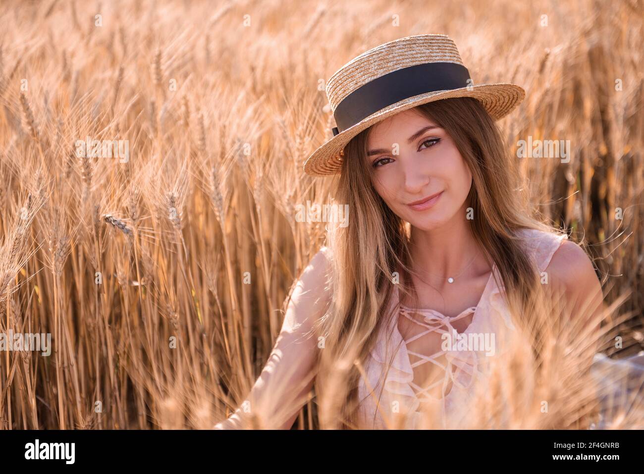 Jeune femme blonde en chapeau de paille sur le fond d'un champ d'épillets dorés de blé, seigle. Gros plan portrait d'une belle fille aux yeux bruns. W Banque D'Images
