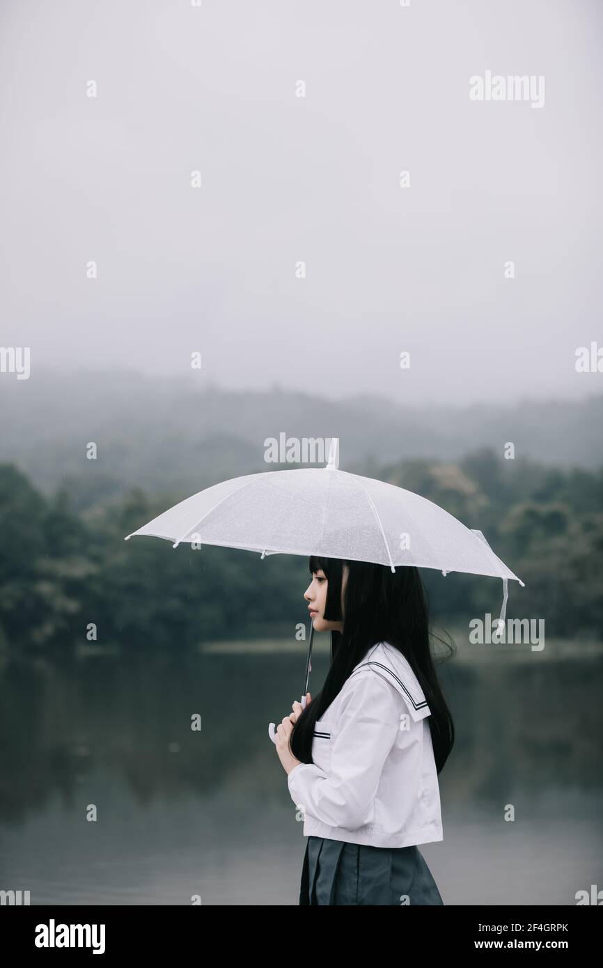 Portrait de fille d'école asiatique regardant avec parapluie au lac en cas de pluie Banque D'Images