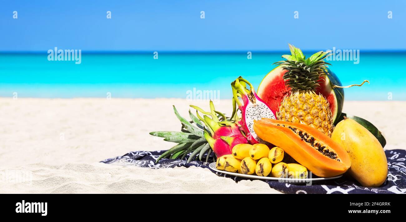 Panorama de différents fruits tropicaux frais placés sur la plage avec ciel bleu et fond de mer. Plage d'été concept de saine alimentation. Banque D'Images