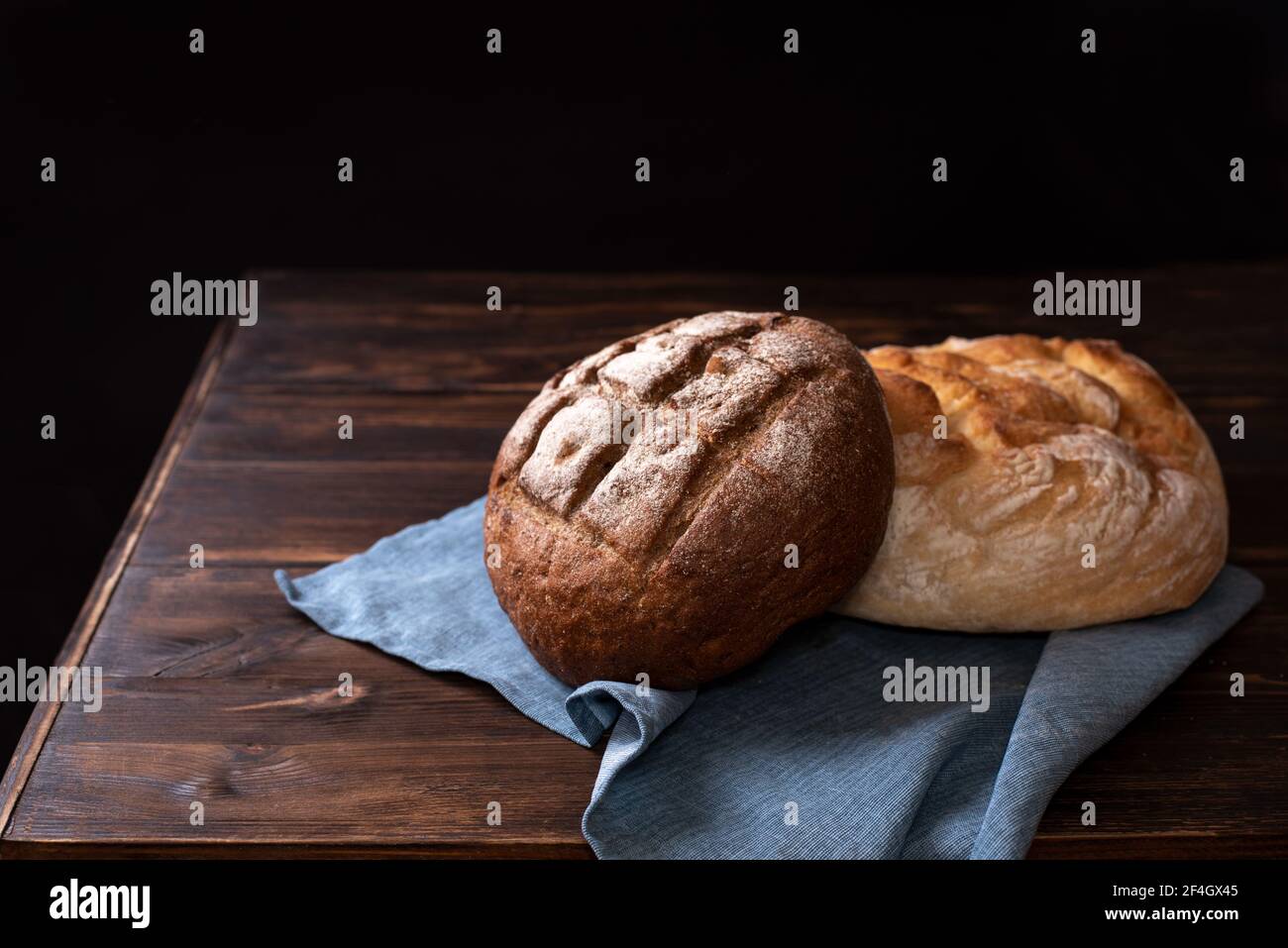 Pains ronds de seigle et de blé de pain sur une table en bois avec une serviette sur fond noir, style rustique, gros plan. Banque D'Images