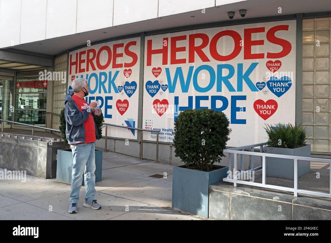 Un homme qui attend dans la file d'attente au Lenox Health Greenwich Village pour obtenir sa vaccination Covid-19 en regardant un panneau sur le bâtiment qui dit « les héros travaillent ici ». 20 mars 2021 Banque D'Images