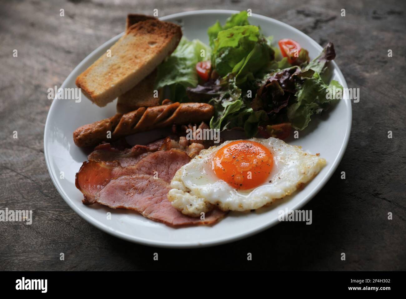 Petit déjeuner anglais frit œufs, jambon, saucisse, bacon, salade et toasts sur fond de bois dans la lumière mystique Banque D'Images