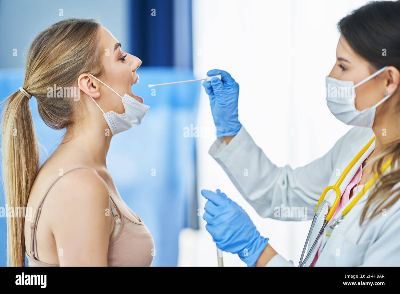 Médecin dans le masque en train de prélever un écouvillon de gorge de sa patiente Banque D'Images