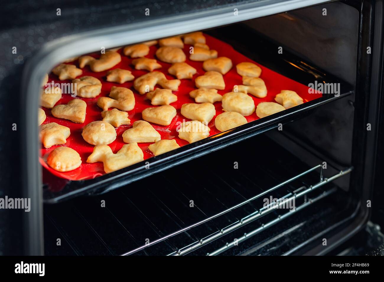 Délicieux et savoureux petits gâteaux au gingembre cuit dans une cuisinière chaude sur un plateau et un tapis de boulangerie en silicone rouge vif dans la cuisine maison. Biscuits chauds faits maison Banque D'Images