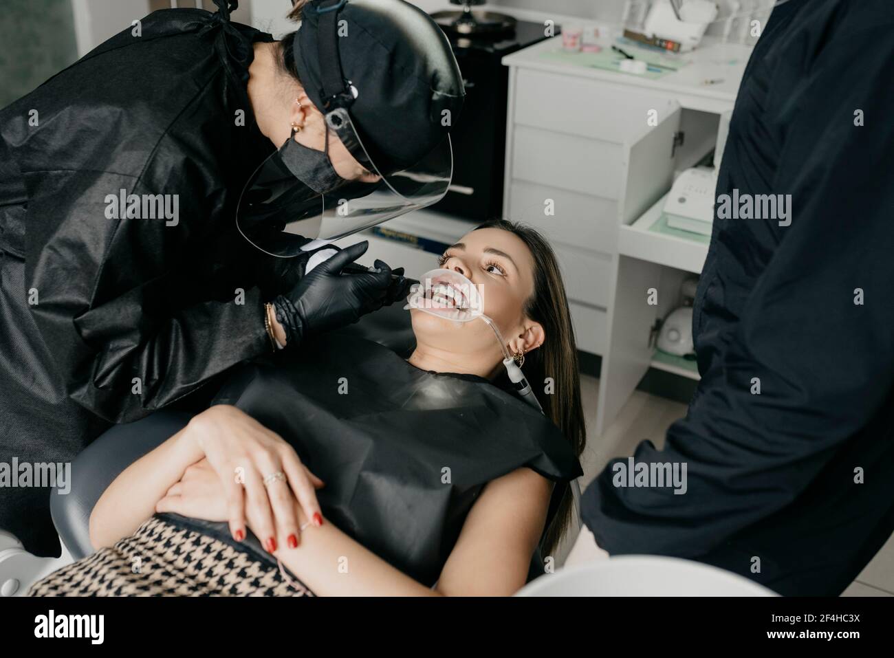 Grand angle de la patiente avec enrouleur et éjecteur de salive dans la bouche regardant le dentiste pendant l'intervention dentaire en clinique Banque D'Images Grand angle de la patiente avec enrouleur et éjecteur de salive dans la bouche regardant le dentiste pendant l'intervention dentaire en clinique Banque D'Images