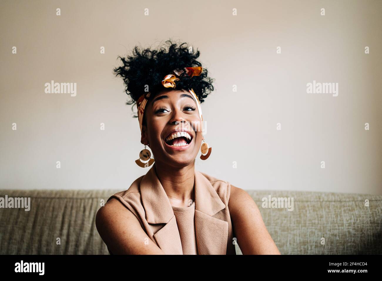 Femme afro-américaine joyeuse avec bandeau tendance et afro coiffer assis  sur le canapé en riant tout en regardant loin de la maison Photo Stock -  Alamy