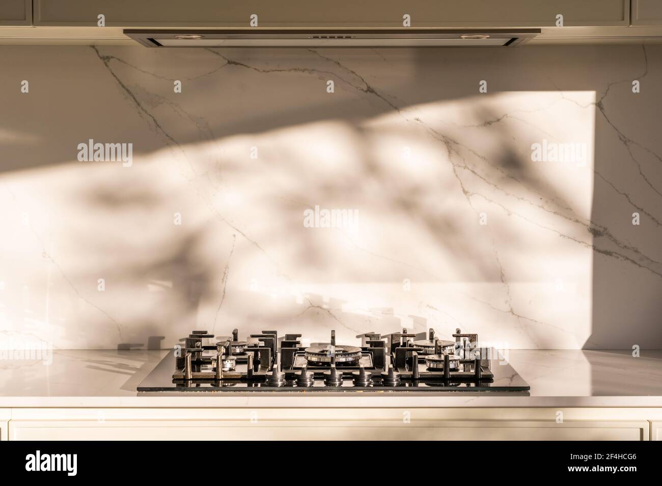 Une table de cuisson moderne au gaz inoxydable et une hotte dans une maison lumineuse cuisine avec mur en marbre Banque D'Images