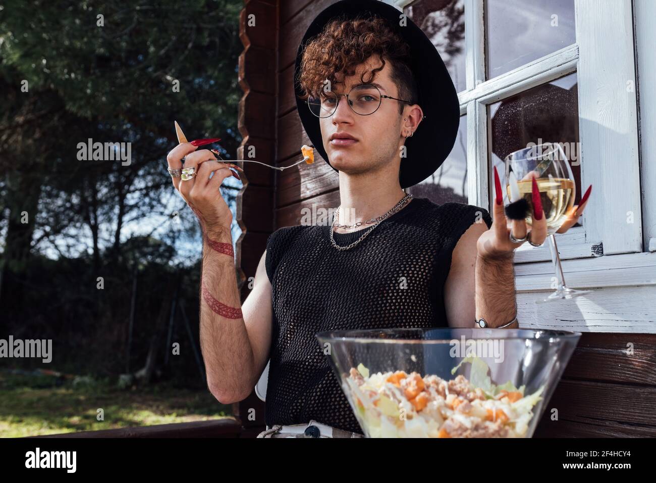 Les jeunes gays sont branchés et assis à la table avec de la nourriture contre bungalow et vin blanc regardant la caméra Banque D'Images