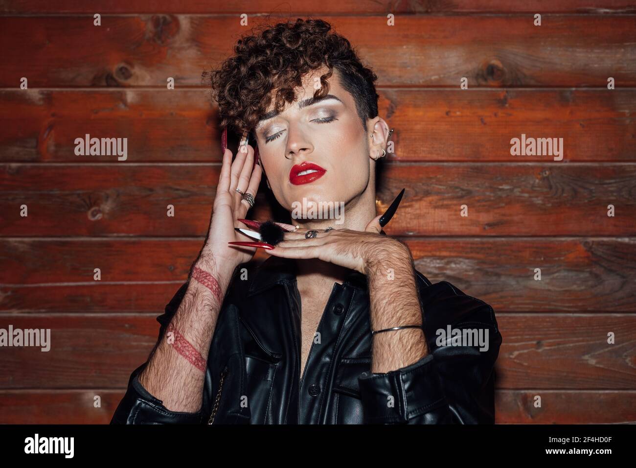 Jeune homme transsexuel tendance avec de longs ongles et des yeux fermés contre le mur en bois dans le chalet Banque D'Images