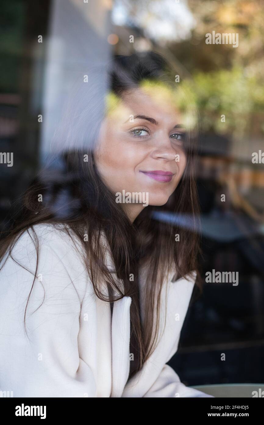 Par la fenêtre de Happy élégant long cheveux femme souriant et regarder l'appareil photo tout en se reposant dans un café Banque D'Images