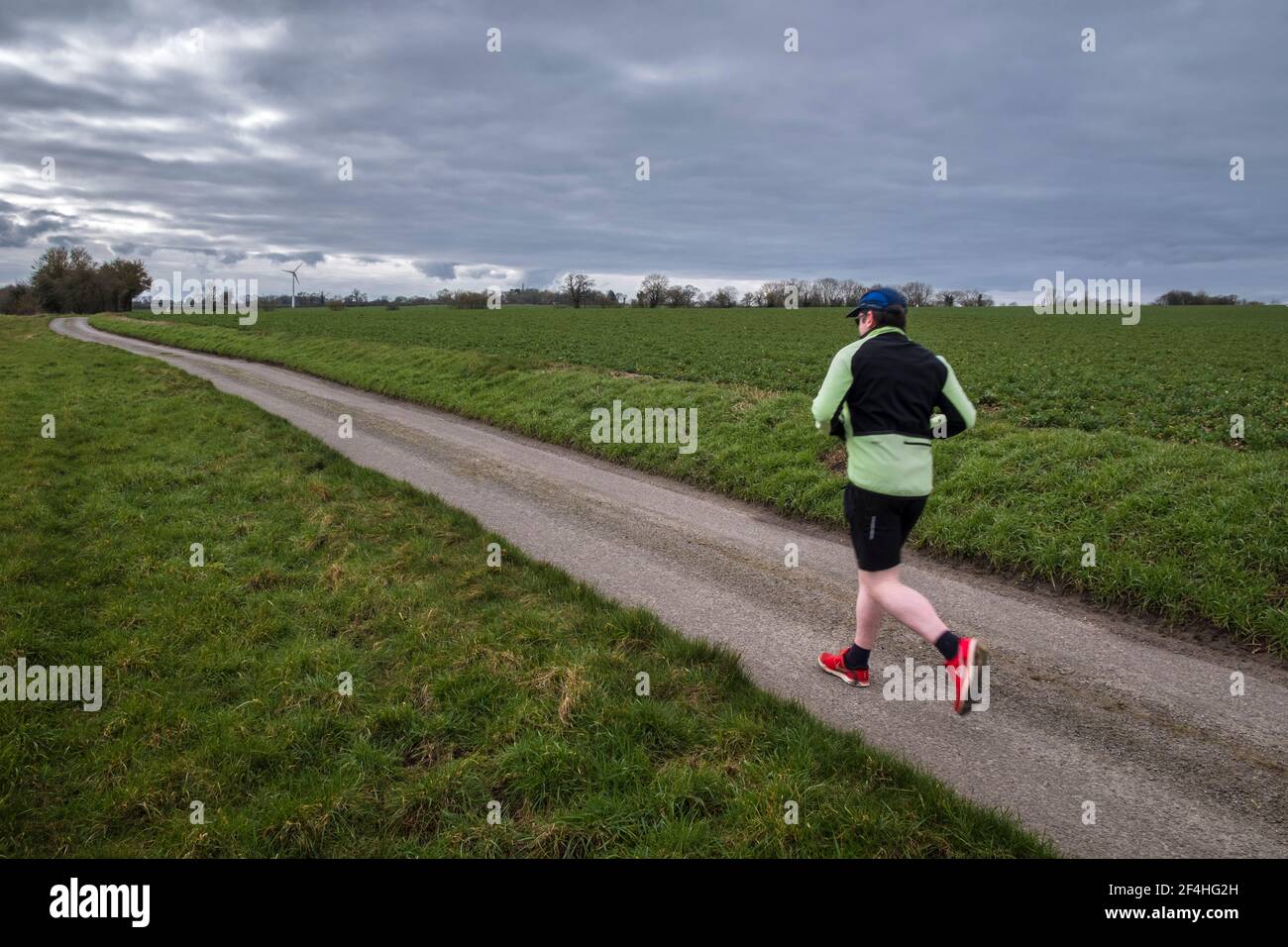 Un coureur de sexe masculin s'exerçant seul à l'extérieur, sur une voie de campagne tôt le matin. Suffolk, Royaume-Uni. Banque D'Images